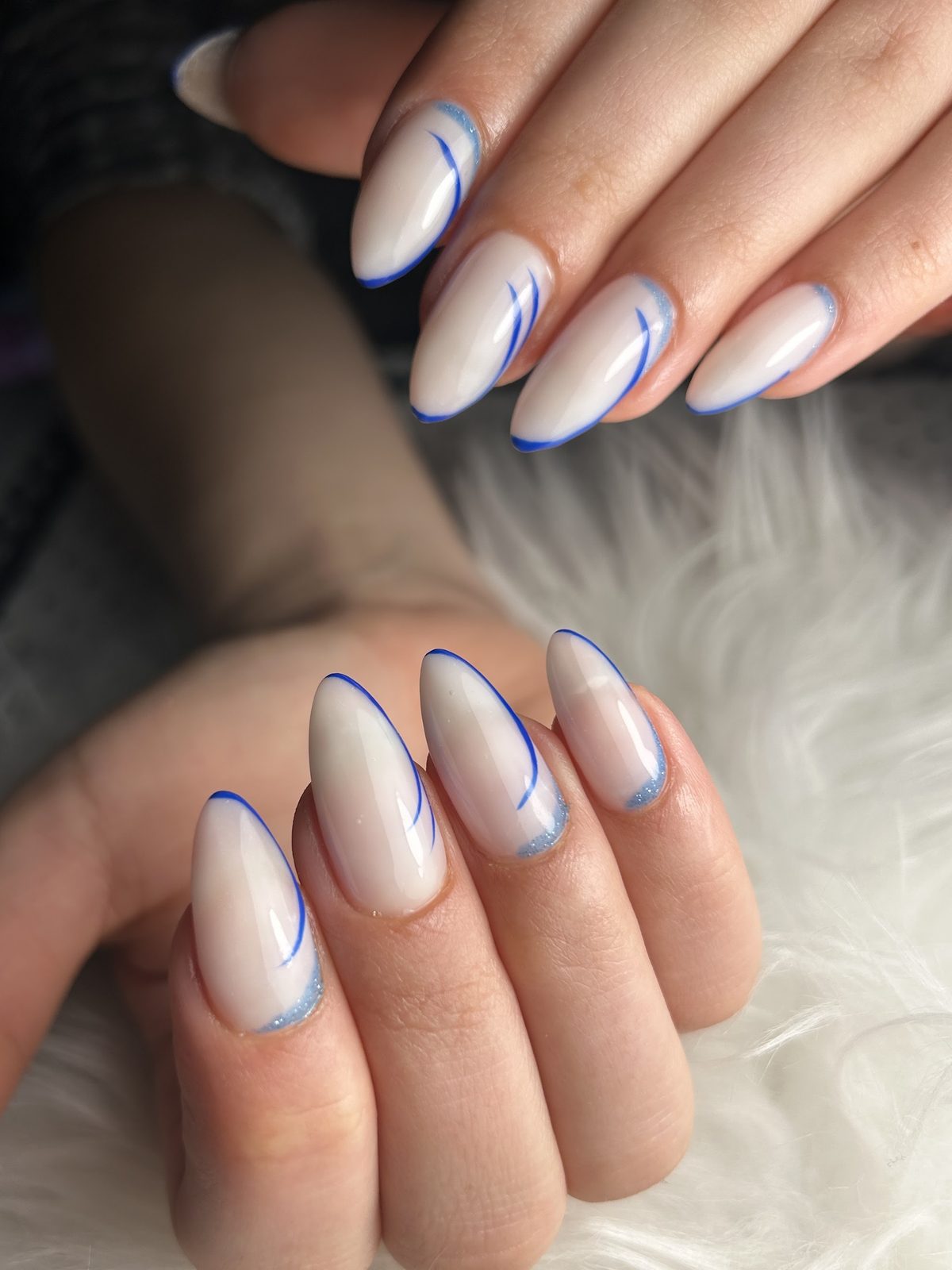 Melkwitte amandelnagels met sierlijke blauwe lijnen, op wit bont