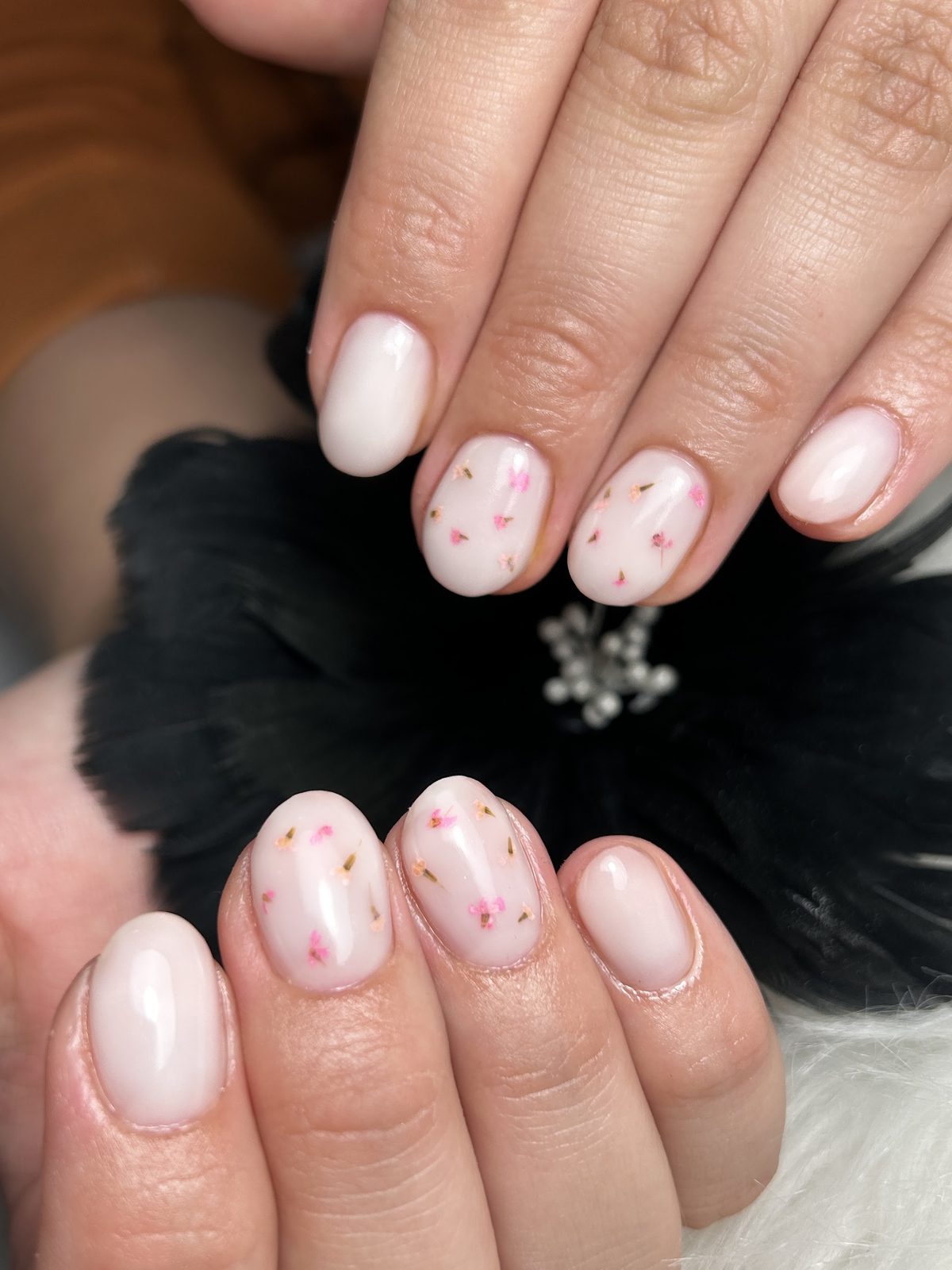 Korte melkwitte nagels met kleine roze bloesemstipjes, op zwart bont